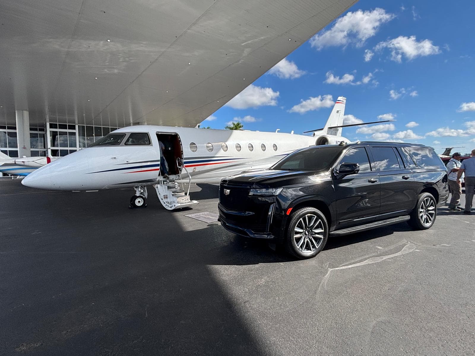 Chauffeur waiting beside a black sedan at a private jet terminal in Miami